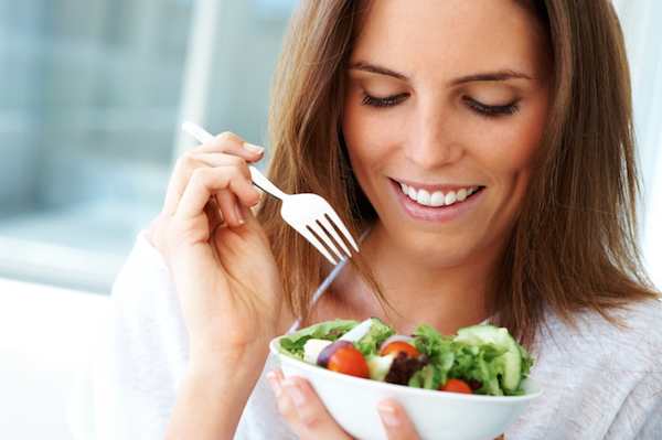 Closeup portrait of a happy young lady eating fruit salad