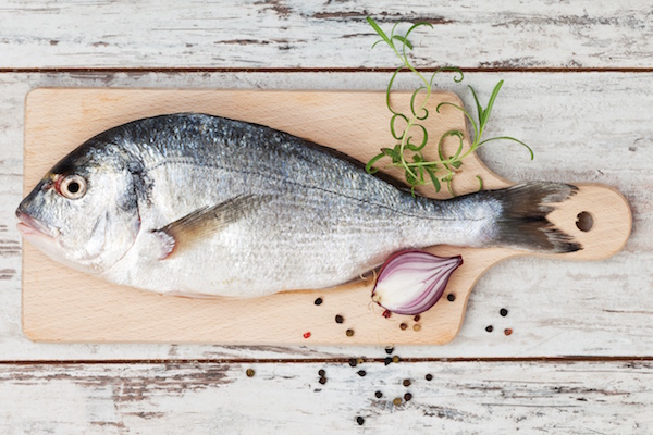 14886299 - delicious fresh sea bream fish on wooden kitchen board with onion, rosemary and colorful peppercorns on white textured wooden background  culinary healthy cooking